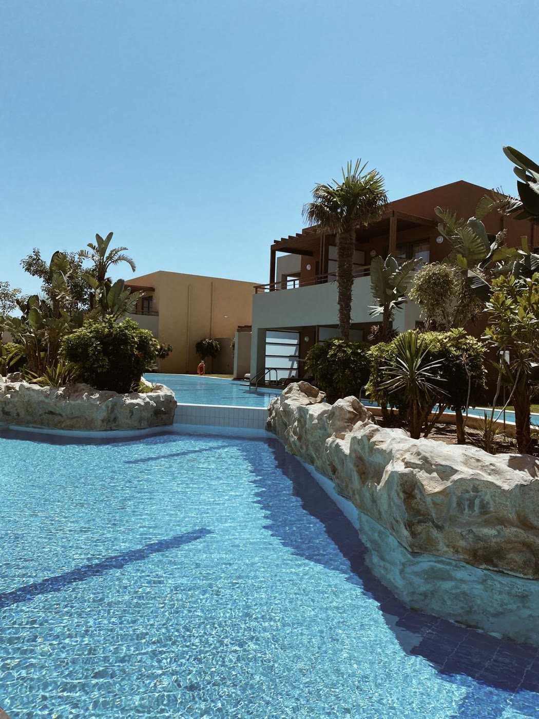 Weitläufige Poollandschaft mit Felsen und Palmen vor den Suiten des Astir Odysseus
