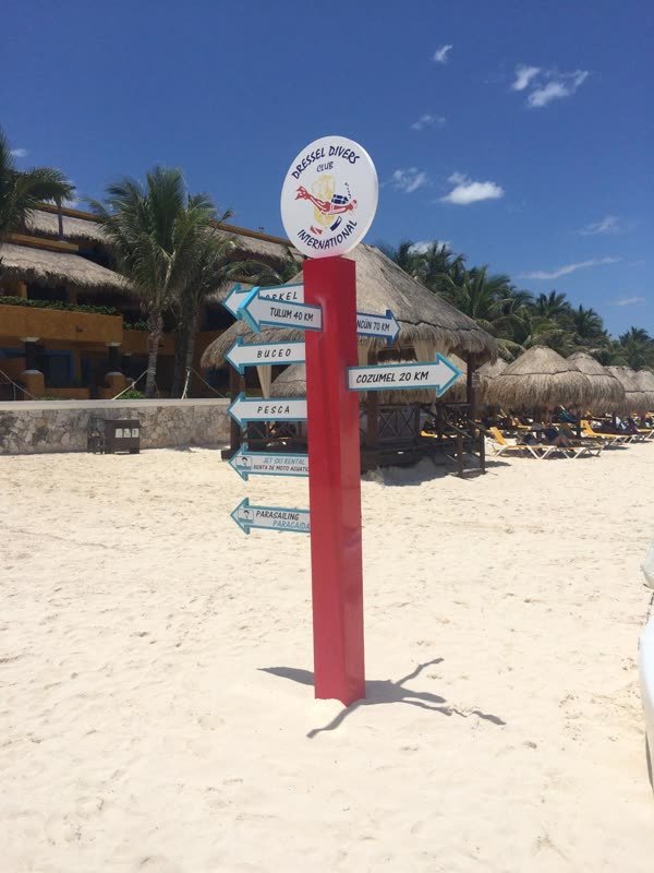 Wegweiser der Tauchbasis am Strand mit Entfernungen nach Tulum und Cozumel